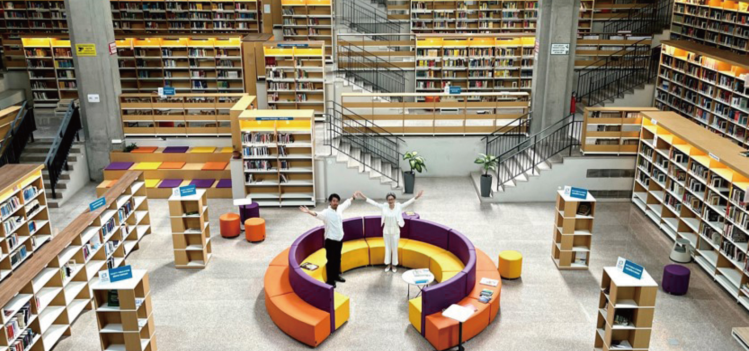 吹き抜けのある図書館の中央にある円形のソファで手を広げて並ぶ2人