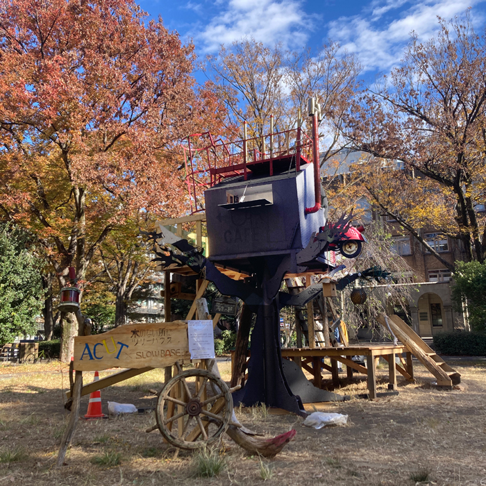 「ACUT 木のない所にツリーハウス」という立て看板と、赤いスクーターが突き刺さった赤色と青紫色のツリーハウス