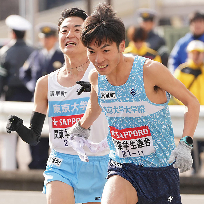 「関東学生連合」のゼッケンをつけた秋吉選手と古川選手が白いタスキをつなぐ様子
