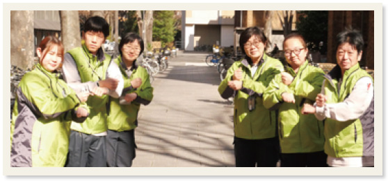 緑色の作業服を着た6人が手話で「おつかれさま」のポーズをとり集合写真に映る様子